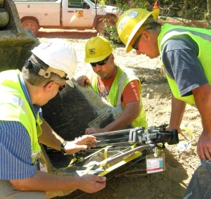 Representatives of Geiger Brothers and its subcontractor secure a camera to the excavator bucket to capture images of the soil composition and layering structure in the narrow 27-foot-deep trench.